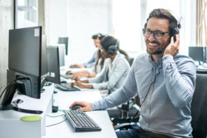 Man working on computer with headphones on smiling with people in background working on computers