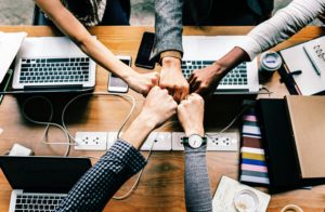 5 individuals with arms reaching in over laptops